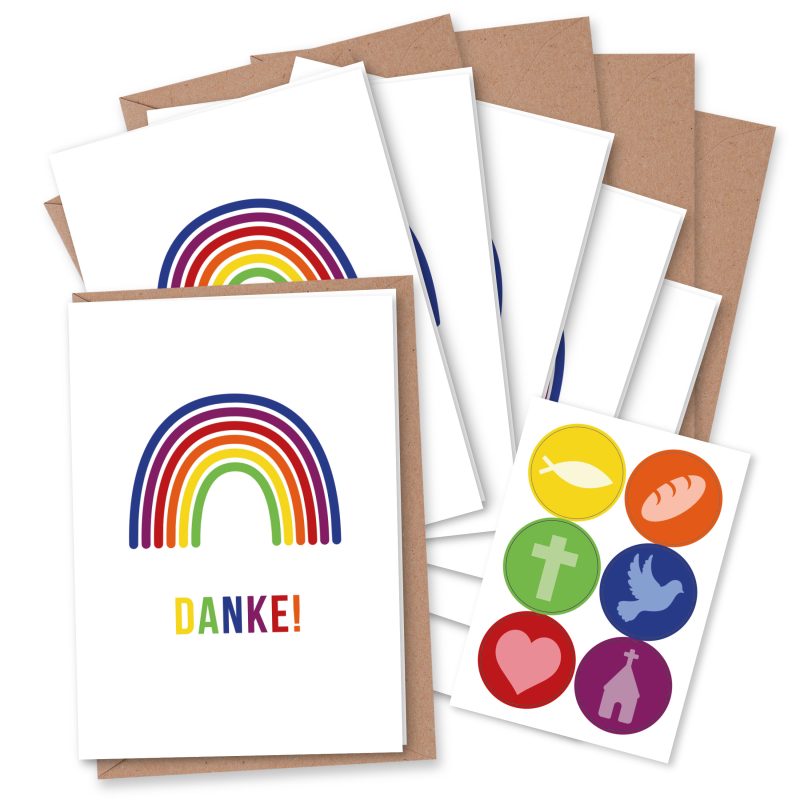 Grußkartenstapel mit Regenbogen und der Aufschrift Danke neben Stickern mit christlichen Symbolen in leuchtenden Farben auf weißem Hintergrund