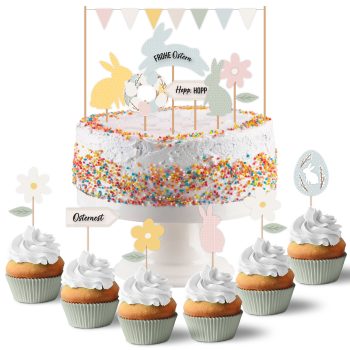 Osterkuchen mit bunter Zuckerstreusel-Dekoration auf Tortenständer, umgeben von Cupcakes mit Sahne-Topping und Osterschmuck wie Hasen, Eiern und Blumen aus Papier