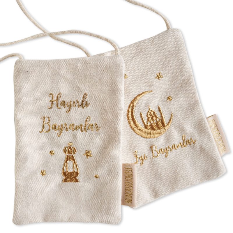 Zwei beige Geschenkbeutel mit goldenen Stickereien, auf dem ersten steht 'Hayırlı Bayramlar' neben einem bestickten Leuchter, auf dem zweiten ein Halbmond und Stern mit 'İyi Bayramlar' Text, türkische Grußworte zum Fest