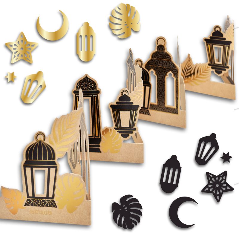Verschiedene goldene und schwarze Papierausschnitte mit Motiven von Laternen, Sternen, Mond und Monstera-Blättern auf hellbraunem Hintergrund im Scrapbooking-Stil
