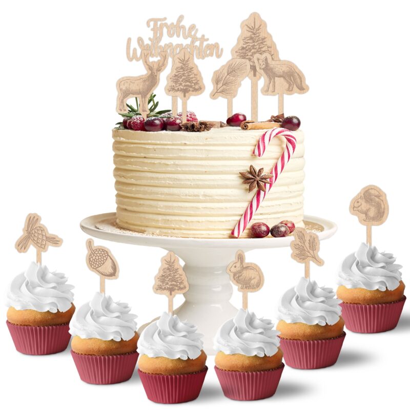 Mehrschichtige Torte mit weißem Frosting und weihnachtlicher Dekoration auf Tortenständer neben Cupcakes mit Waldtier-Motiven und Schriftzug Frohe Weihnachten